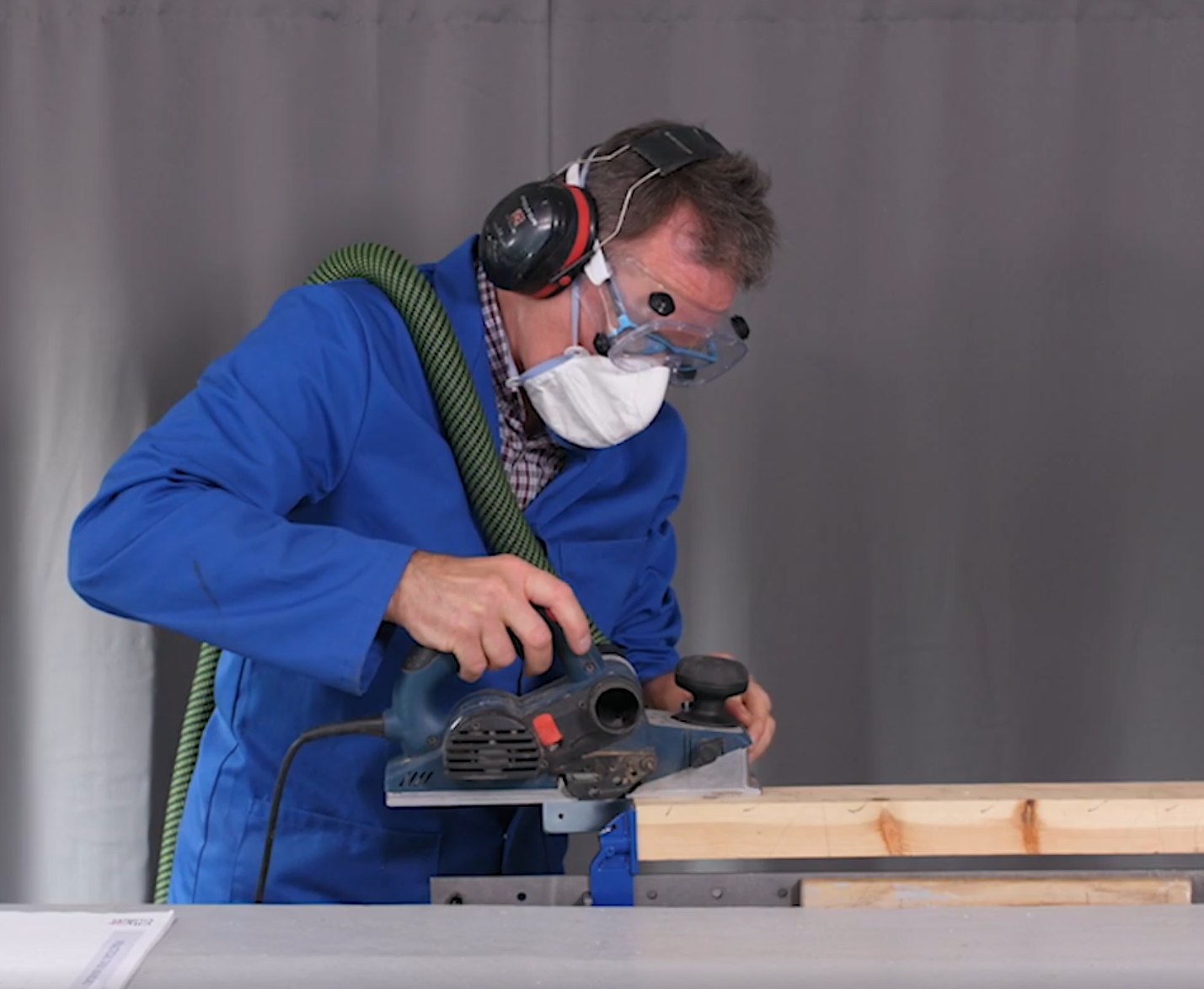 Paul demonstrating a power planer on timber in a workshop, wearing full PPE